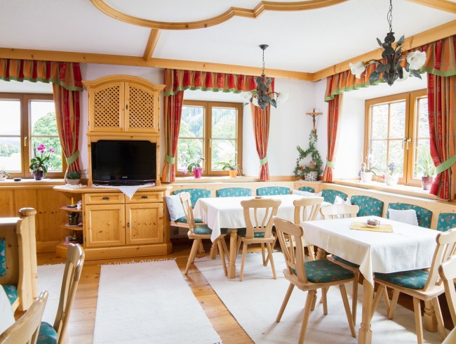 Gemütliche Stube mit Holzmöbeln, Tischen, Stühlen und Blick auf grüne Landschaft durch Fenster
