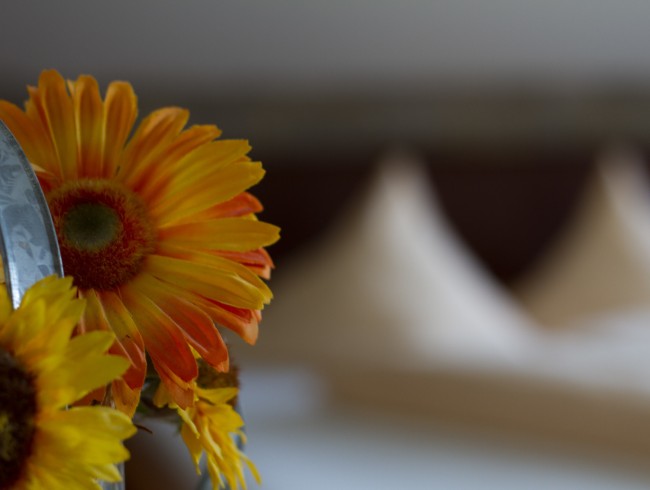 Sonnenblume im Vordergrund, weiches Doppelbett im Hintergrund