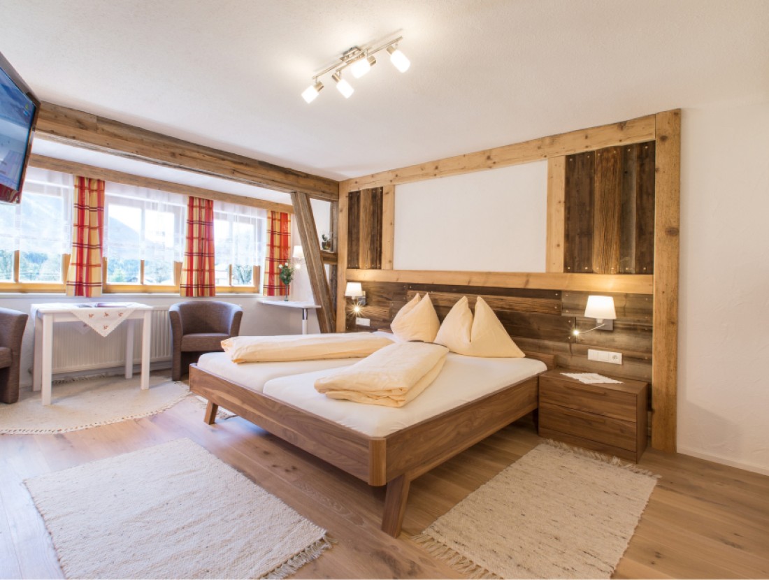 Gemütliches Schlafzimmer mit Doppelbett, Holzwänden und großem Fenster mit Bergblick
